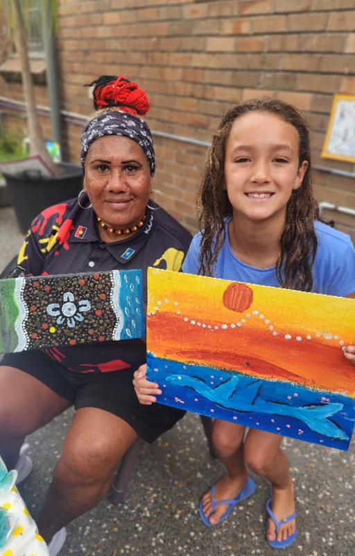 Artist Jude Jarrett and child, smiling holding art session paintings